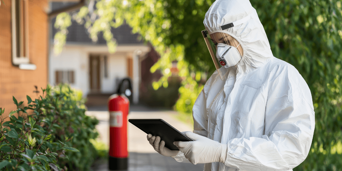 How Smart Pest Monitoring Helps Detect Infestations Before They Become Costly 1 Two individuals in protective suits stand beside a large rock in an outdoor setting.